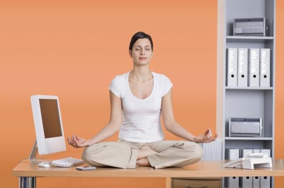 Woman sitting on desk next to computer meditating